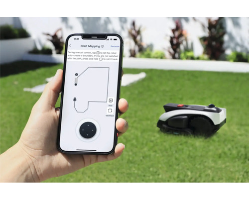 Persoon houdt smartphone met app voor de bediening van een gazonmaaierrobot in de hand. Op de achtergrond bevindt zich de gazonmaaierrobot op een gazon.