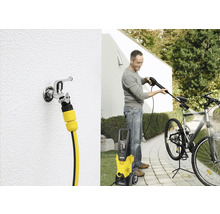 Een man maakt een fiets schoon met een Kärcher hogedrukreiniger. Ook is een waterkraan met slangaansluiting te zien.