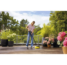 Vrouw reinigt houten terras met een terrasreiniger in de open lucht, omgeven door potplanten.