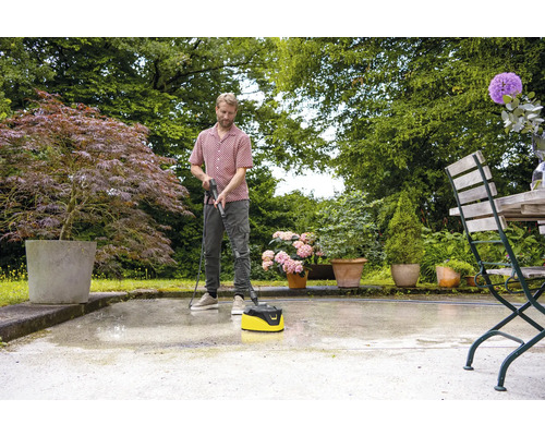 Een man reinigt een terras met een terrasreiniger in de tuin.