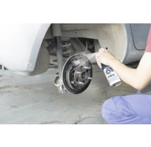 Een persoon reinigt een open trommelrem van een auto met remmenreiniger.