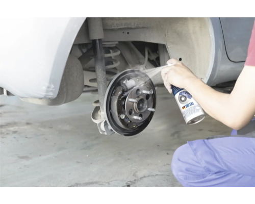 Een persoon reinigt een open trommelrem van een auto met remmenreiniger.