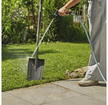 Een persoon maakt een tuinschep schoon met een tuinslang buitenshuis.