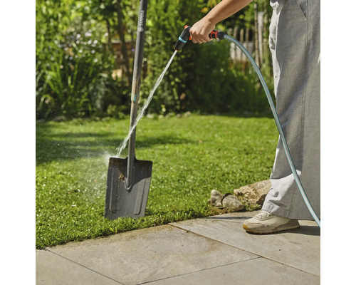 Een persoon maakt een tuinschep schoon met een tuinslang buitenshuis.