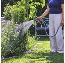 Een persoon besproeit planten in de tuin met een tuinslang.