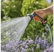 Een hand houdt een tuinslang met sproeikop vast die water op bloemen spuit.