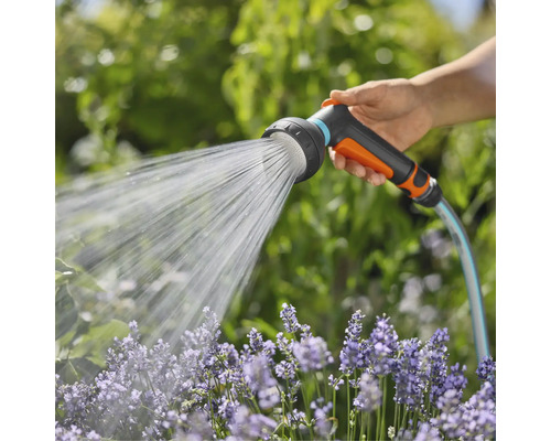 Een hand houdt een tuinslang met sproeikop vast die water op bloemen spuit.
