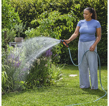 Vrouw besproeit planten met tuinslang in de tuin.