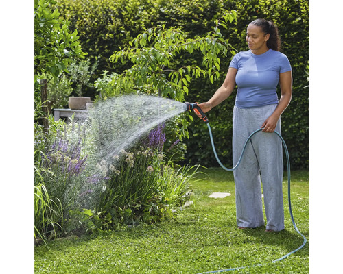 Vrouw besproeit planten met tuinslang in de tuin.