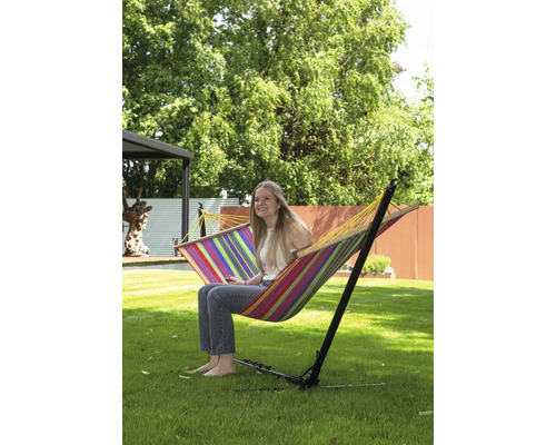 Vrouw zit in een gestreepte hangmat met frame in de tuin.