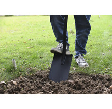 Een persoon gebruikt een spade in de tuin om aarde om te spitten.