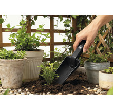 Tuinscène met plantenpotten, omliggend groen en een persoon die een plantenschep gebruikt.