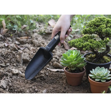 Tuinschep met markeringen in gebruik naast planten in potten.