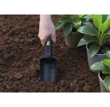Een hand houdt een plantenschep in de aarde, naast potplanten.