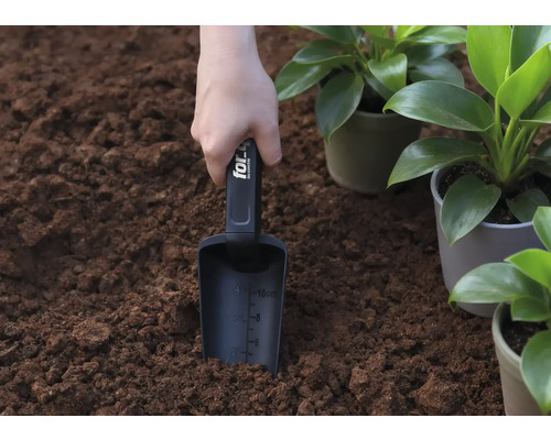 Een hand houdt een plantenschep in de aarde, naast potplanten.