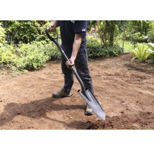 Man houdt spade in de tuin vast.