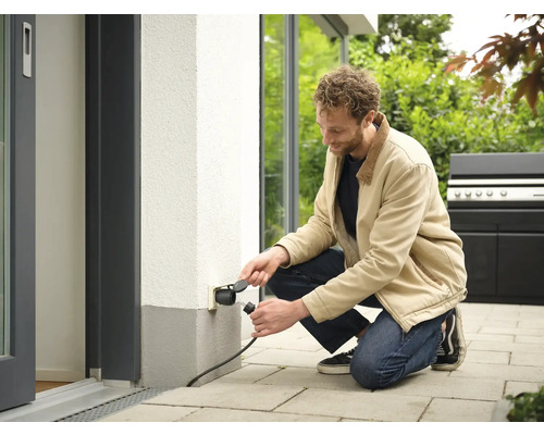 Man sluit stekker aan op stopcontact buiten