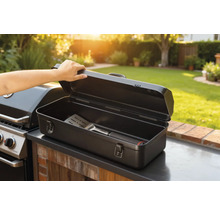 Open barbecuebestekdoos met spatel naast barbecue in de tuin.