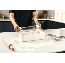 Scene in een keuken: een man opent een vershouddoos met deeg, omringd door bloem, een deegroller en uitsteekvormen.