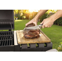 Bereide steak wordt met een mes op een houten plank naast een barbecue gesneden.