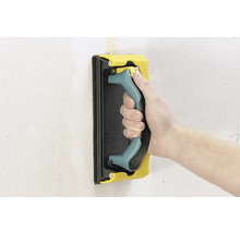 Hand met schuurpad voor het schuren van een muur