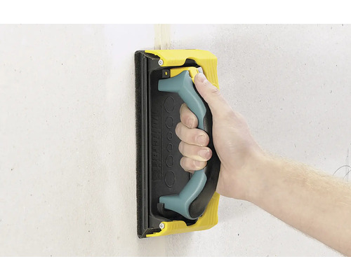 Hand met schuurpad voor het schuren van een muur