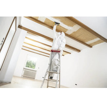 Ambachtsman op een ladder die renovatiewerkzaamheden uitvoert aan een plafond in een heldere ruimte.