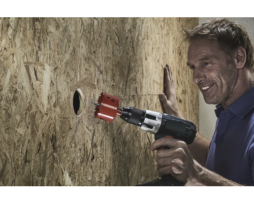 Een man boort een gat in een houten plaat met een gatenzaag.