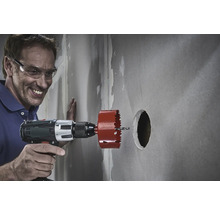 Man boort met een gatzaag een gat in een muur.