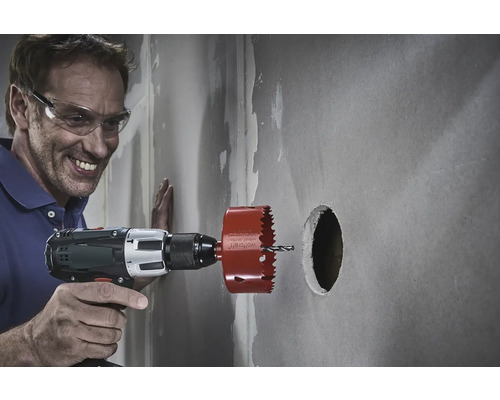 Man boort met een gatenzaag een gat in een muur.