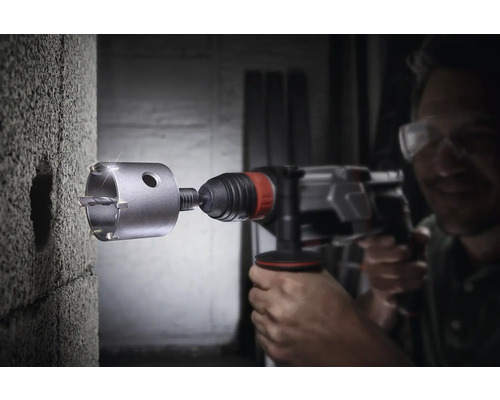 Man boort met een gatzaag een gat in een muur.