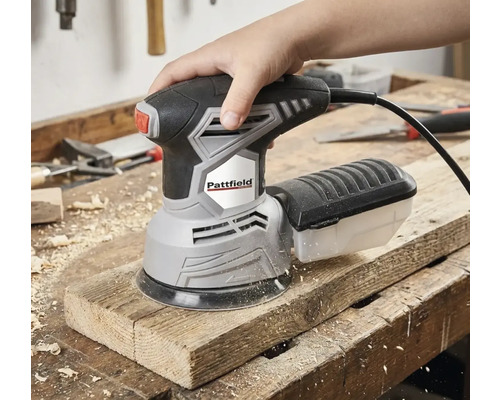 Een hand bedient een Pattfield excentrische schuurmachine op een houten plank.