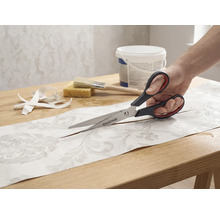 Een persoon snijdt een stuk behang met patroon doormidden met een Rautner schaar op een tafel