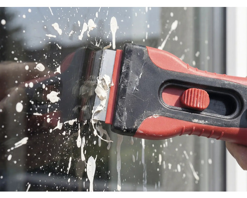 Verfschraper in gebruik voor het verwijderen van verfspatten op glas.