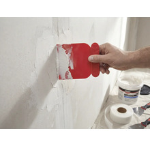 Een man brengt een rode plamuurmes aan op een muur met glasvezeltape