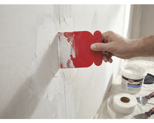 Een man brengt een rode plamuurmes aan op een muur met glasvezeltape