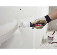 Ambachtsman plamuurt muur met plamuurmes en vulmiddel. Rautner Logo zichtbaar.