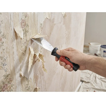 Een persoon verwijdert met een plamuurmes oud behang van een muur.