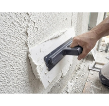 Vakman brengt gips aan op een muur met een pleisterspaan.