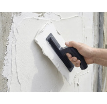 Een persoon brengt met een pleisterspaan pleister aan op een muur.