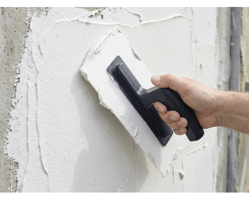 Een persoon brengt met een pleisterspaan pleister aan op een muur.