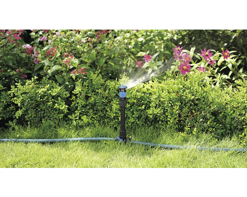 Tuinscene met gazonsproeier die planten besproeit