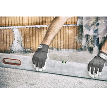 Een persoon die met een waterpas en werkhandschoenen een muur van bakstenen uitlijnt