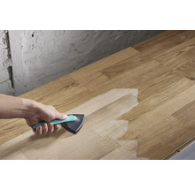 Iemand brengt een oppervlaktebehandeling aan met een driehoekige kwast op een houten plank.