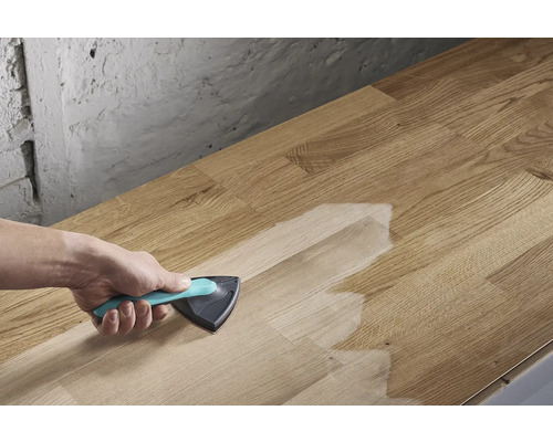 Iemand brengt een oppervlaktebehandeling aan met een driehoekige kwast op een houten plank.