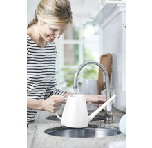 Vrouw vult een witte gieter aan de kraan in de keuken.