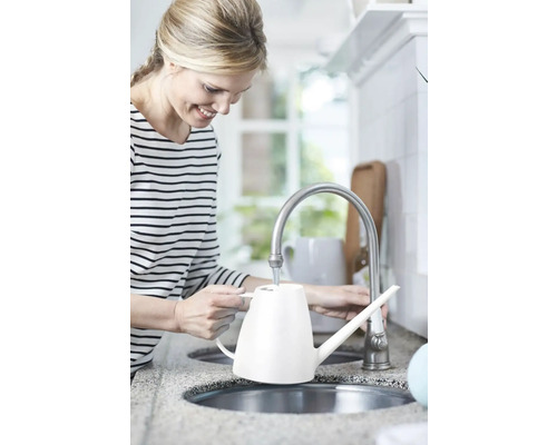 Vrouw vult een witte gieter aan de kraan in de keuken.