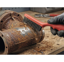 Een persoon verwijdert roest van een metalen buis met een draadborstel.