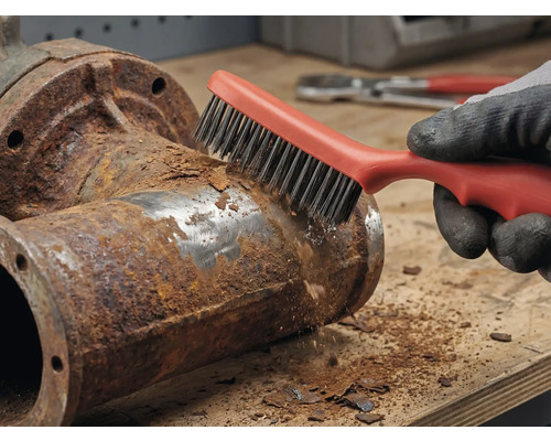 Een persoon verwijdert roest van een metalen buis met een draadborstel.