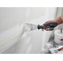 Een persoon plamuurt een muur met plamuur en een plamuurmes van Rautner.